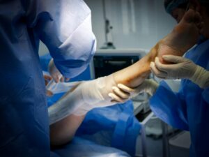 Surgical team in blue gowns and gloves work together, holding a patient’s arm during an operation in a sterile OR.