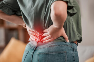 Person presses both hands against the lower back, showing back pain with a red glow at the lumbar area in casual clothing and jeans.