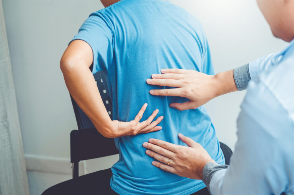 Physiotherapist placing hands on a person’s back for assessment in a clinic.