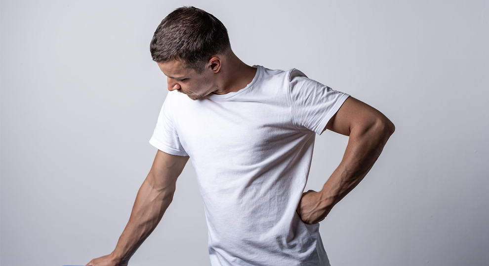 Man in a plain white T-shirt stands against a light gray background, his left hand on his hip and head tilted downward for a casual pose.