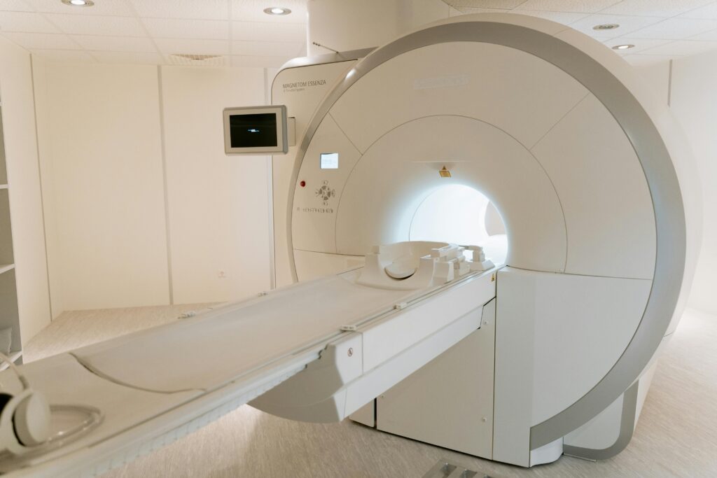 MRI scanner in a quiet radiology room with patient table and a wall-mounted monitor nearby.
